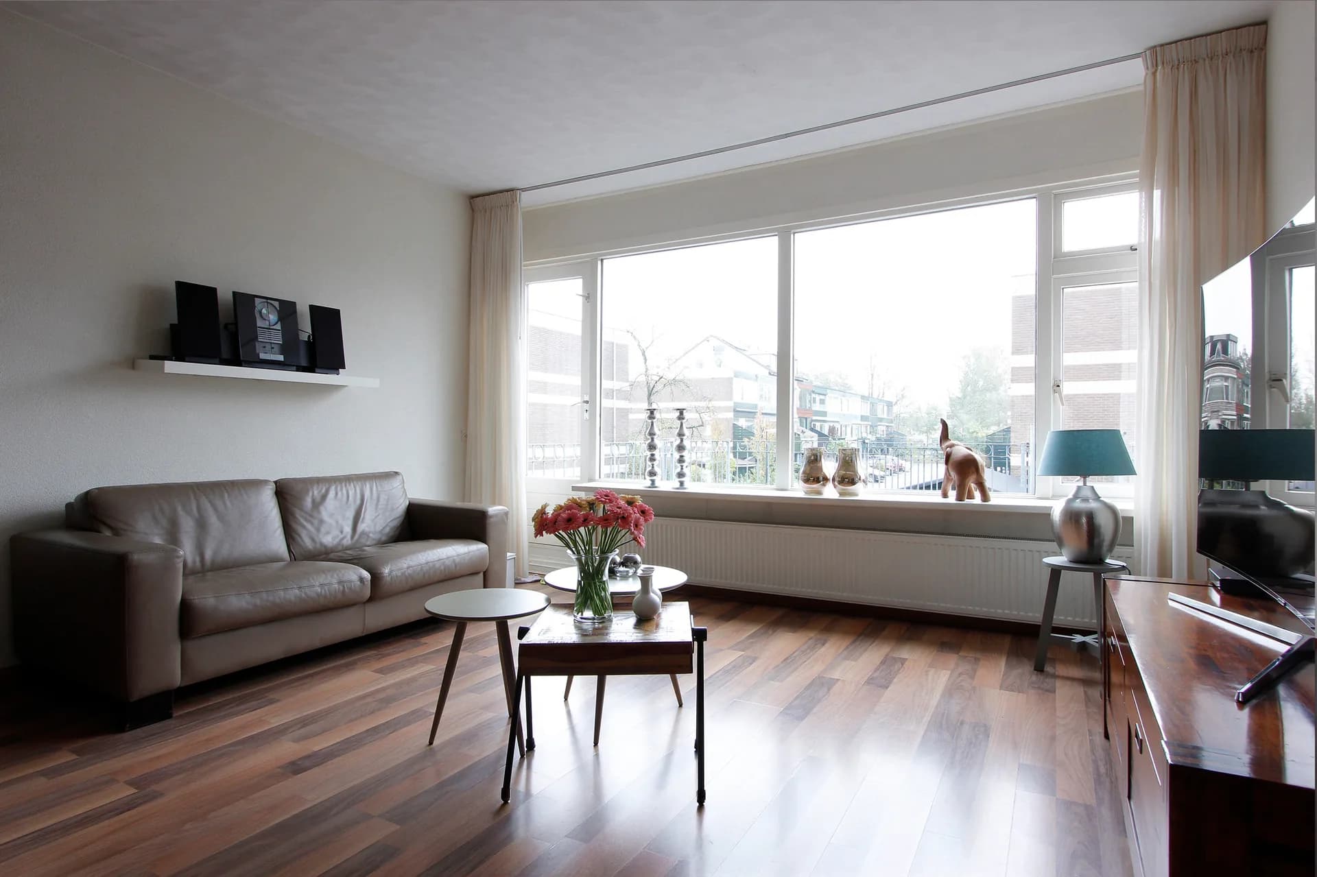Living room before editing, with a dark sofa and a bright window view